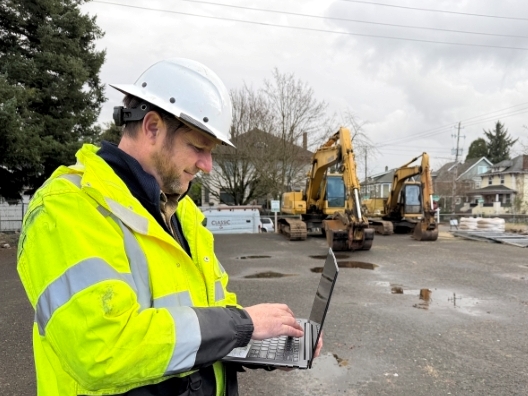 Construction site supervisor John in high-visibility gear working on laptop at the Alberta Alive Townhomes project in Northeast Portland.
