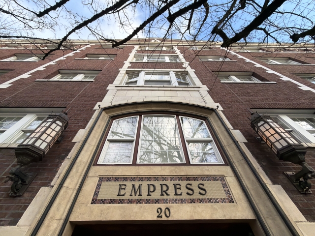 Dramatic upward view of the entrance facade of the Empress Condominiums at 20 NW 16th Avenue in Northwest Portland, Oregon. Built in 1927 as the Empress Hotel, this five-story brick building was later converted to condominiums. The photo emphasizes the tiled signage, arched window, and vintage lanterns in the Nob Hill/Alphabet District.
