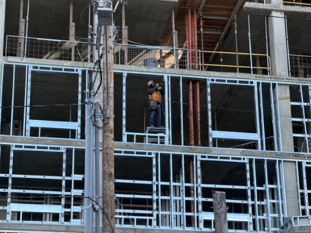 Construction worker using drill on steel framing of hollywoodHUB affordable housing tower at Hollywood Transit Center, Northeast Portland – January 12, 2026 – skilled labor on upper scaffolding level.